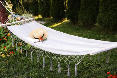 Straw hat, glasses, book and flowers on hammock outdoors