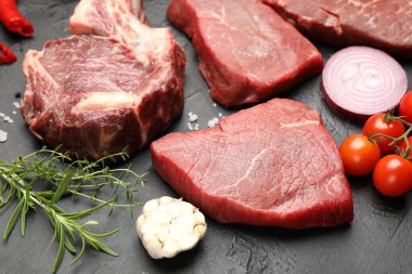 Çiğ et parçaları, baharatlar ve domatesler siyah masada, yakın plan.