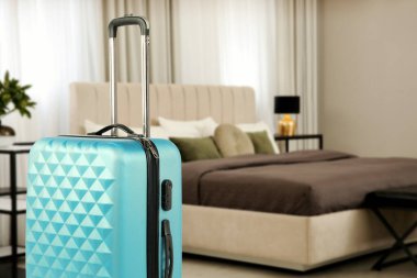 Hotel room with large bed and guest suitcase, selective focus