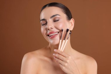 Kahverengi arka planda makyaj fırçası olan güzel bir kadın.