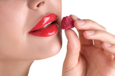 Dudaklarında güzel kırmızı ruj ve beyaz arka planda ahududu şekeri olan kadın, yakın plan.