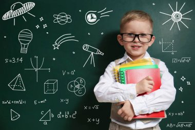 Yeşil karatahtanın yanında gözlük takan, formüllü ve çizimli bir çocuk.