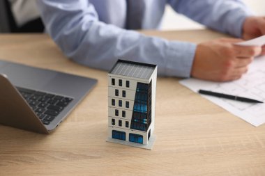 Evrak işleriyle uğraşan emlakçı, apartman modeli ve dizüstü bilgisayarı ahşap masada, yakın plan.