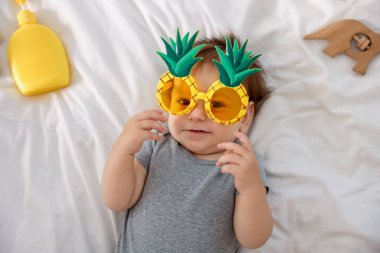 Yatağında güneş gözlüğü ve aksesuarları olan sevimli bir bebek.