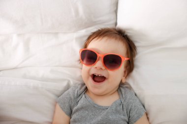 Güneş gözlüklü komik bebek yatağında yatıyor.
