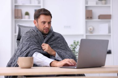 Klima. Ofiste battaniyeli bir adam soğuk hava yüzünden acı çekiyor.