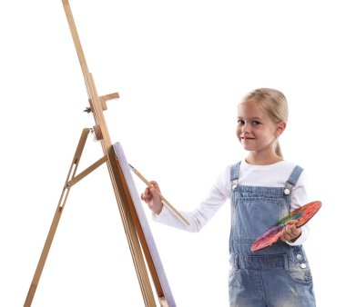 Meslek seçimi. Beyaz arka planda ressammış gibi davranan palet boyalı ve sehpanın yanındaki fırçalı küçük kız.