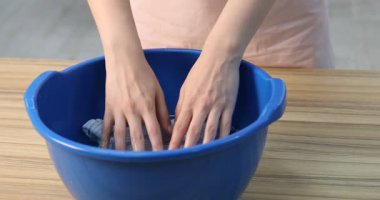 Kadın bebek çamaşırlarını leğende yıkıyor ahşap masada, kapalı alanda, yakın plan.