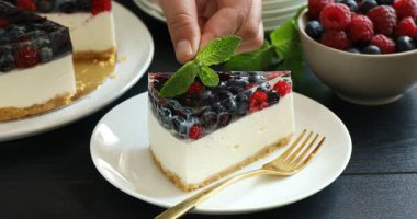 Siyah ahşap masada naneli, nefis dutlu cheesecake süsleyen kadın.