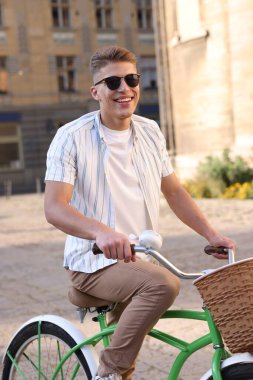 Şehir caddesinde bisiklet süren güneş gözlüklü mutlu adam.