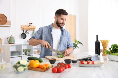 Mutfakta yemek pişirirken tabletten yemek tarifine bakan gülümseyen adam.