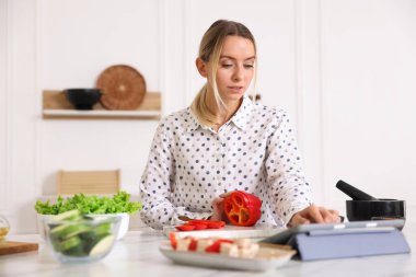 Mutfakta yemek pişirirken tabletten yemek tarifine bakan güzel bir kadın.