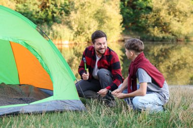 Mutlu baba ve oğul nehir kenarında kamp çadırı kuruyorlar.