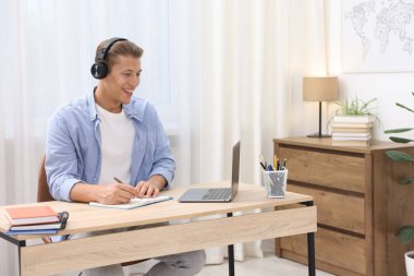 Kulaklıklı bir adam, içerideki masada dizüstü bilgisayarla sınavdan geçerken not alıyor.