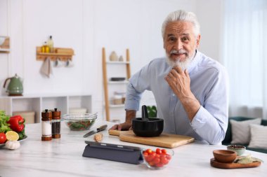 Mutfaktaki beyaz mermer masada yaşlı bir adam yemek pişiriyor.