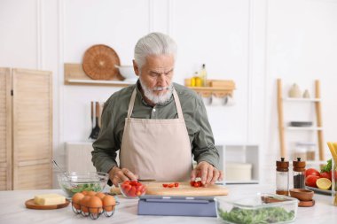 Mutfaktaki beyaz mermer masada yaşlı bir adam yemek pişiriyor.