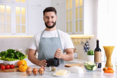 Mutfaktaki masada yemek pişiren gülümseyen adam.