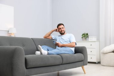 Evdeki kanepede akıllı telefonlu bir adam.