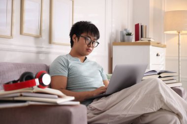 Bilgisayarlı gözlüklü öğrenci ve evdeki kanepede sınava hazırlanan kitaplar.