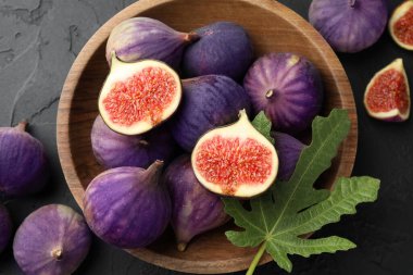 Fresh ripe figs and green leaf in bowl on black table, top view