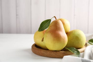 Fresh ripe pears and green leaves on white wooden table, closeup. Space for text