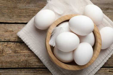 Raw chicken eggs and feathers on wooden table, top view. Space for text