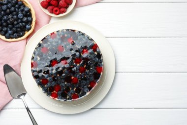 Delicious cheesecake with berries and cake server on white wooden table, flat lay. Space for text