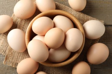 Raw chicken eggs in bowl on wooden table, flat lay