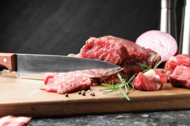 Pieces of raw beef meat, spices and knife on black marble table, closeup