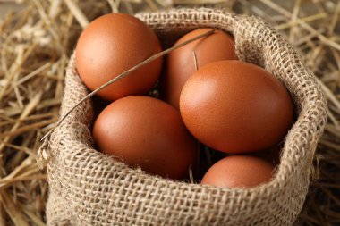 Raw chicken eggs in burlap sack on straw, closeup