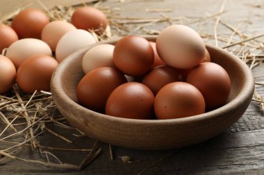 Tabakta çiğ tavuk yumurtası ve ahşap masada saman, yakın plan.