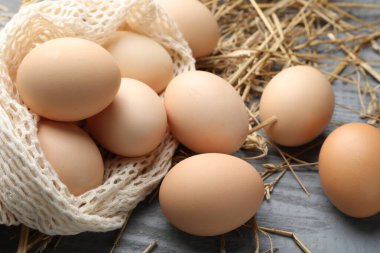 Çiğ tavuk yumurtası, ağ torbası ve saman gri ahşap masa, yakın plan.