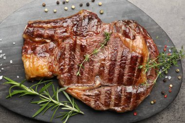 Gri desenli masa üzerinde baharatlı ve otlu ızgara biftek.