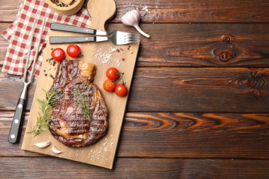 Delicious grilled beef steak with herbs, spices and products on wooden table, flat lay. Space for text