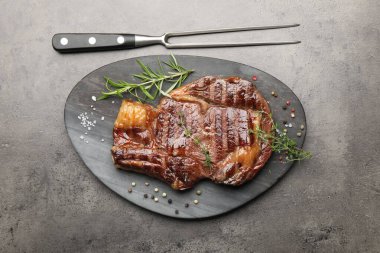 Lezzetli ızgara biftek, otlar, baharatlar ve çatal, gri desenli masa, düz yatış.