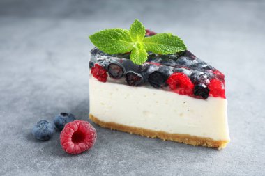 Piece of delicious cheesecake with berries and mint on grey table, closeup