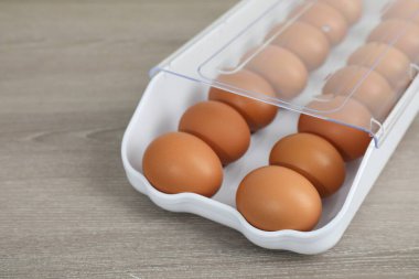 Raw chicken eggs in plastic container on wooden table, closeup. Space for text