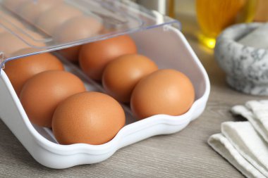 Plastik kabın içinde çiğ tavuk yumurtası ve ahşap tezgahın üzerinde mutfak aletleri, yakın plan.