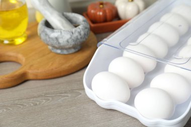 Plastik kabın içinde çiğ tavuk yumurtası ve ahşap tezgahın üzerinde mutfak aletleri, yakın plan.