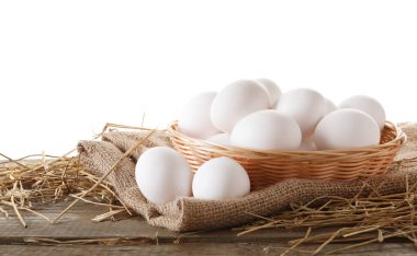 Çiğ tavuk yumurtası, hasır sepet, beyaz arka plana karşı ahşap masa ve saman