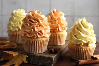 Renkli kremalı lezzetli kekler ve ahşap masada sonbahar dekoru, yakın plan.