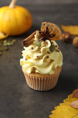 Delicious cupcake with color cream, spices and autumn decor on grey table, closeup