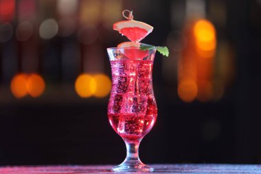 Glass of alcoholic cocktail with garnish on table against blurred background, bokeh effect