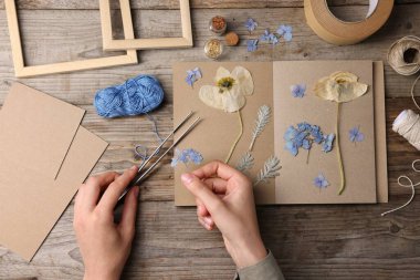 Ahşap masa, üst manzara, kuru çiçekleri deftere koyan kadın.