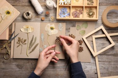 Ahşap masa, üst manzara, kuru çiçekleri deftere koyan kadın.