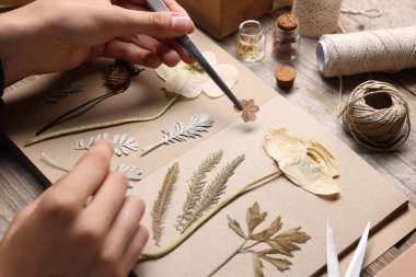 Ahşap masadaki kuru çiçekleri deftere koyan kadın, yakın plan.