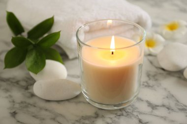 Beautiful spa composition with burning candle on white marble table, closeup