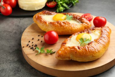 Tasty khachapuris with cheese, eggs, tomatoes and spices on grey textured table, closeup