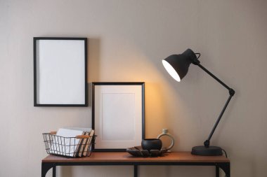 Stylish lamp, other decor and books on console table near beige wall indoors