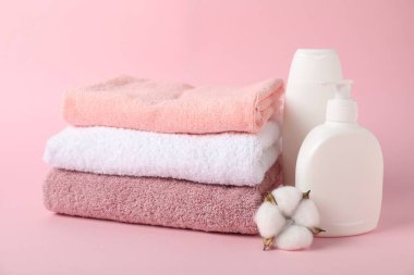 Bir yığın taze havlu, kozmetik ürünler ve pembe arka planda pamuk.